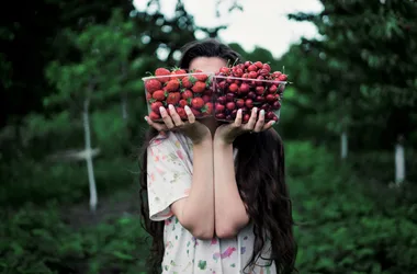 The girl holds two boxes filled with strawberries and cherries against the backdrop of the garden. Conception: choice food vegan