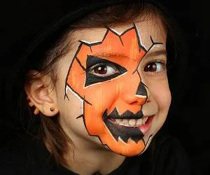 Pretty girl with face painting of a pumpkin isolated on black background